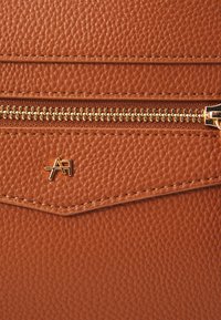 Cartera de cuero texturizado marrón que presenta un cierre de cremallera dorado, un sutil patrón y un acento de logotipo dorado.