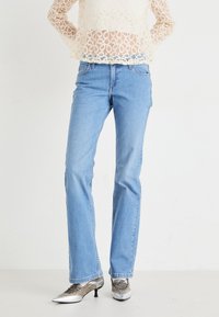 Jeans rectos de color azul claro con un diseño desgastado, estilo clásico de cinco bolsillos y detalles de costura sutiles, combinados con zapatos de tacón plateados.