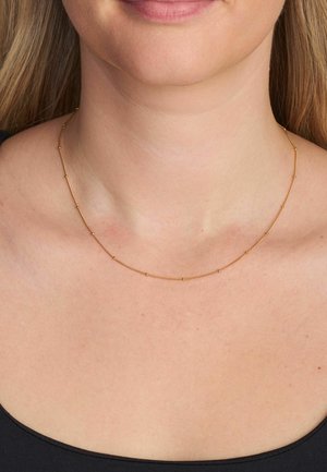 Plāna zelta kaklarota ar mazām cilindriskām pērlītēm un starplikām, izsmalcināts dizains, kas atrodas tieši virs atslēgas kaula.