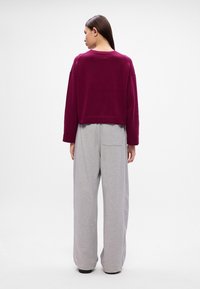 Bordo cropped džemperis ar garajām piedurknēm, saskaņots ar gaiši pelēkiem platām biksēm, kurām ir aizmugurējā kabata. Gluda tekstūra, minimāls dizains.