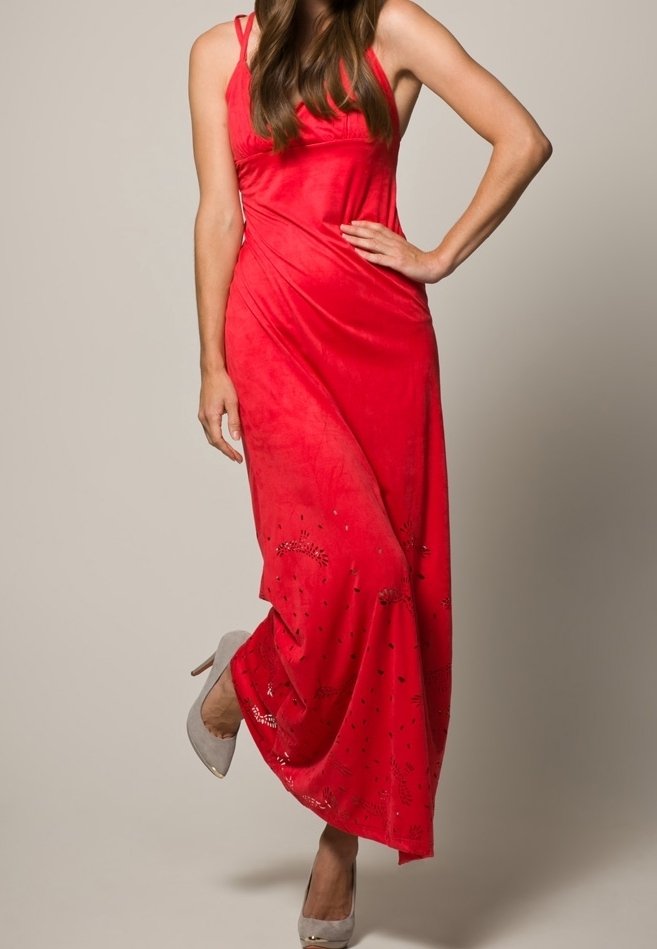 Vestido maxi rojo de tela suave con tirantes finos, que presenta patrones decorativos en el dobladillo. Combinado con zapatos de tacón altos en gris claro.