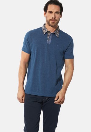 Blaues Polohemd aus strukturiertem Stoff, mit einem gemusterten Kragen mit Knöpfen und kurzen Ärmeln, kombiniert mit dunklen Hosen.