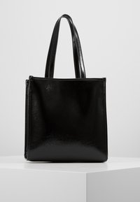 Błyszcząca czarna prostokątna torba tote z dwoma uchwytami, wyeksponowana w pionie na białym cokole na jasnoszarym tle.