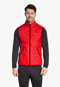 Red quilted vest with high collar, front zip closure, and two zippered side pockets. Worn over a black long-sleeve shirt.