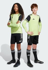 Två barn i idrottskläder. Flickan har en limegrön långärmad topp med svarta detaljer, och pojken har en liknande design. Båda har svarta shorts.