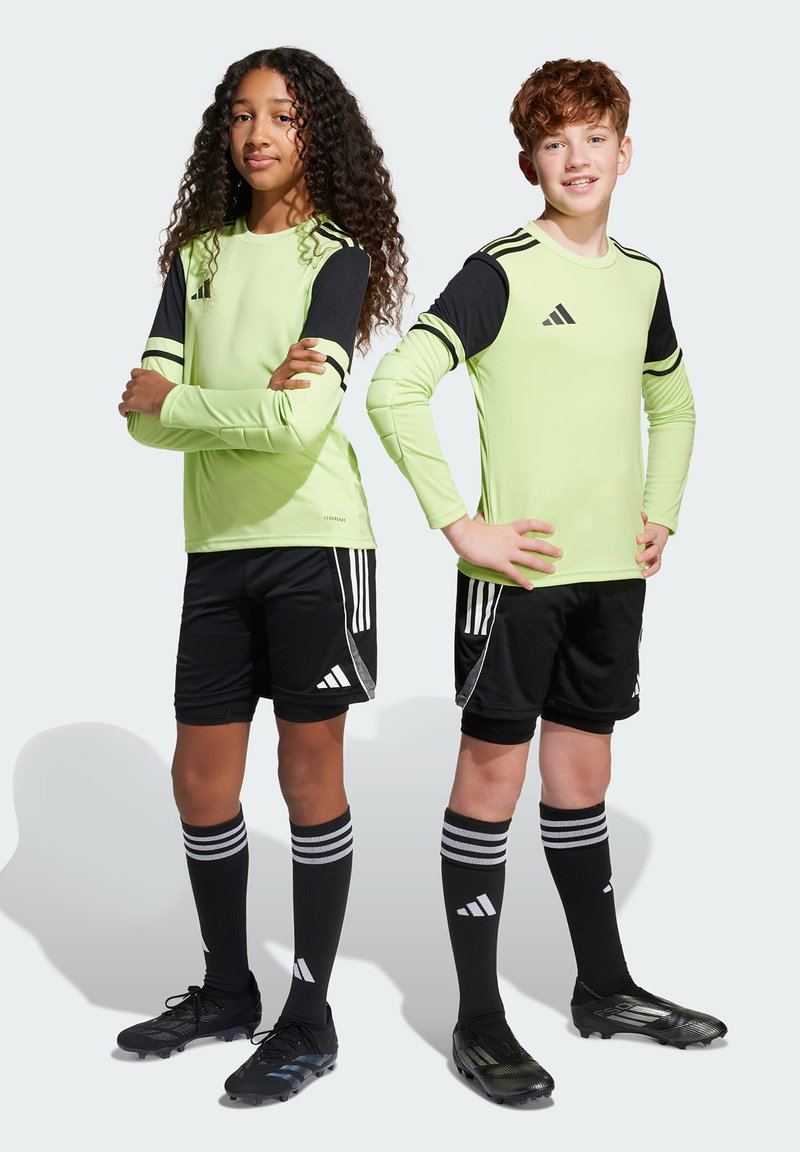 Två barn i idrottskläder. Flickan har en limegrön långärmad topp med svarta detaljer, och pojken har en liknande design. Båda har svarta shorts.