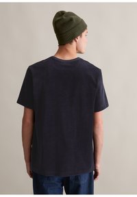 Ciemnoniema koszulka z krótkim rękawem, o luźnym kroju i okrągłym dekolcie. Połączona z zieloną wełnianą czapką, widocznymi szwami, teksturowanym materiałem.