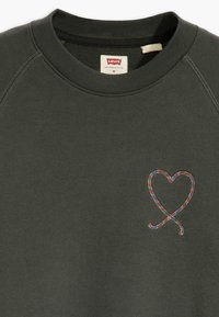 Tmavě zelená mikina s kulatým výstřihem a raglánovými rukávy. Obsahuje barevný vyšívaný design srdce na levé straně hrudi.