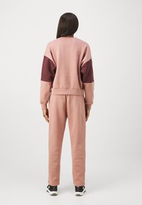 Roza hoodie s bordo detajmi, sproščen kroj, rebrasti manšeti in pas. Usklajene roza trenirke, gladka tekstura, črne športne čevlje.