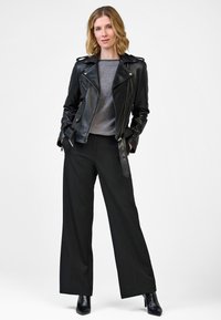 Zwarte leren motorjack met zilveren hardware, grijze trui en zwarte wijde broek. Model draagt puntige zwarte hakken.