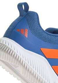 Baskets de sport bleues avec logo et accents orange, semelle blanche texturée et languette de traction au talon.