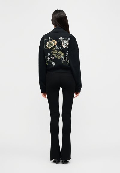 Μαύρο φούτερ με κεντήματα λουλουδιών στην πλάτη, άνετη εφαρμογή, συνδυασμένο με μαύρο παντελόνι καμπάνα. Ομαλή υφή υφάσματος, μακριά μανίκια.