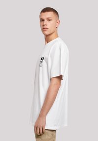 Hvid t-shirt med korte ærmer og et grafisk sort tegnefilmsfigur på brystet. Lavet af blød bomuld med en afslappet pasform.