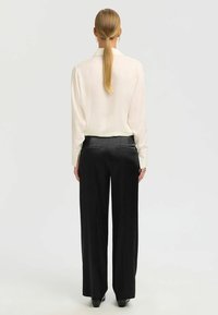 Blouse en soie crème avec un col, associée à un pantalon large noir, présentant une texture lisse et un léger éclat.