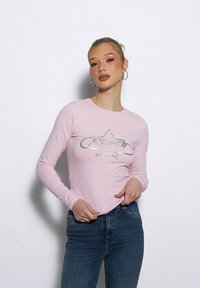 Różowa koszula z długim rękawem z grafiką srebrnej gwiazdy oraz napisanym na niej słowem "SUPER" w wyrazistym kroju. Miękka tkanina o dopasowanym kroju.