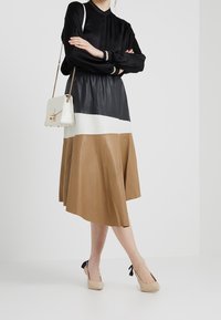 Schwarze Langarmbluse mit Kragen, kombiniert mit einem farblich abgestimmten Lederrock in Schwarz, Weiß und Beige. Beigefarbene High Heels runden das Outfit ab.