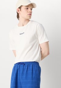 Camiseta blanca de manga corta con el logo "GANT"; pantalones cortos de cintura elástica azul texturizados con cordón. Corte general relajado.