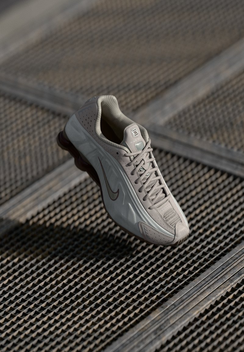 Baskets Nike beiges avec une tige texturée, un système de laçage et une semelle brune contrastante. Détails de design perforé et branding subtil.