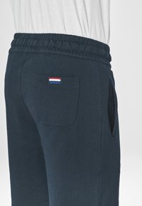 Pantaloni jogger blu marino realizzati in tessuto morbido, dotati di una cintura elastica, tasche laterali e una tasca posteriore applicata con un'etichetta rossa, bianca e blu.
