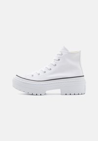Bottines à plateforme en toile blanche avec une semelle en caoutchouc épaisse, un design à lacets et une bande noire le long du bord, présentant une finition texturée.