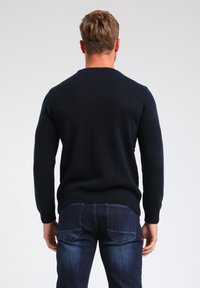 Granatowy sweter dziany z długimi rękawami, żebrowanymi mankietami i dołem, noszony z ciemnoniebieskimi dżinsami. Wzór strukturalny z okrągłym dekoltem.