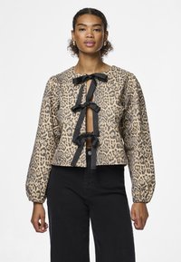 Túnica corta estampada de leopardo em bege e preto, com três laços pretos ao longo da frente e mangas longas bufantes.