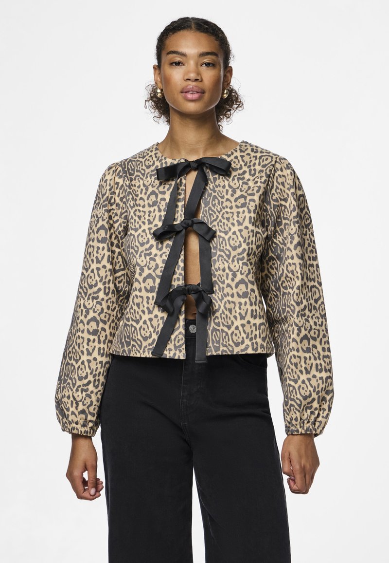 Túnica corta estampada de leopardo em bege e preto, com três laços pretos ao longo da frente e mangas longas bufantes.