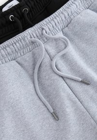 Pantalones de chándal grises con cinturilla elástica negra, con cordones y puntas metálicas. Textura suave y diseño casual.