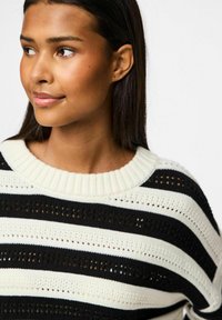 Maglione a righe bianche e nere in maglia con un ampio scollo a coste e un motivo di punto aperto, che conferisce un aspetto testurizzato.