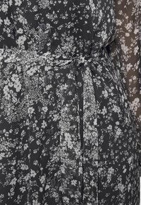 Vestido negro con estampado floral blanco, con botones en la parte delantera y un cinturón de tela a juego atado en la cintura, con mangas largas y transparentes con flores.