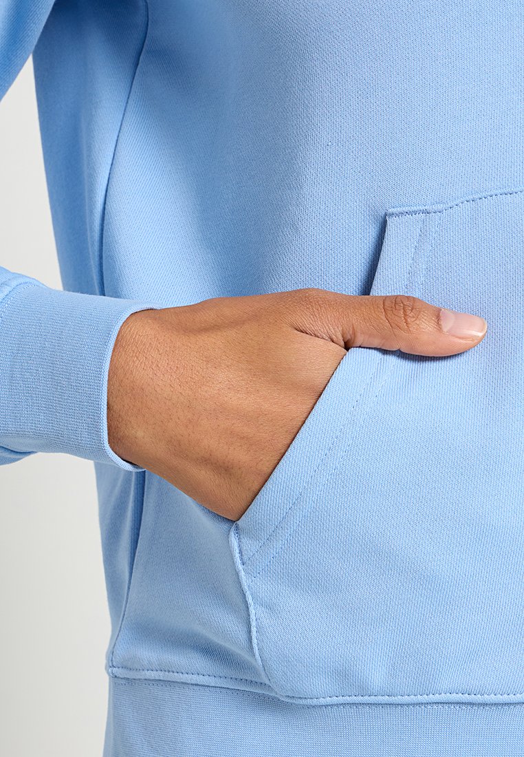 Jasnoniebieska bluza z kapturem o miękkiej, teksturowanej tkaninie. Posiada kieszeń z przodu oraz dopasowane ściągacze, co podkreśla jej smukły i sportowy design.