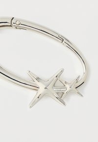 Bracelet en argent avec deux breloques en forme d'étoile, une plus grande et une plus petite, sur un fond blanc uni.
