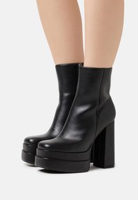 Black leather ankle boots with a smooth texture, high block heels, and a platform sole. Features a side zipper for closure.