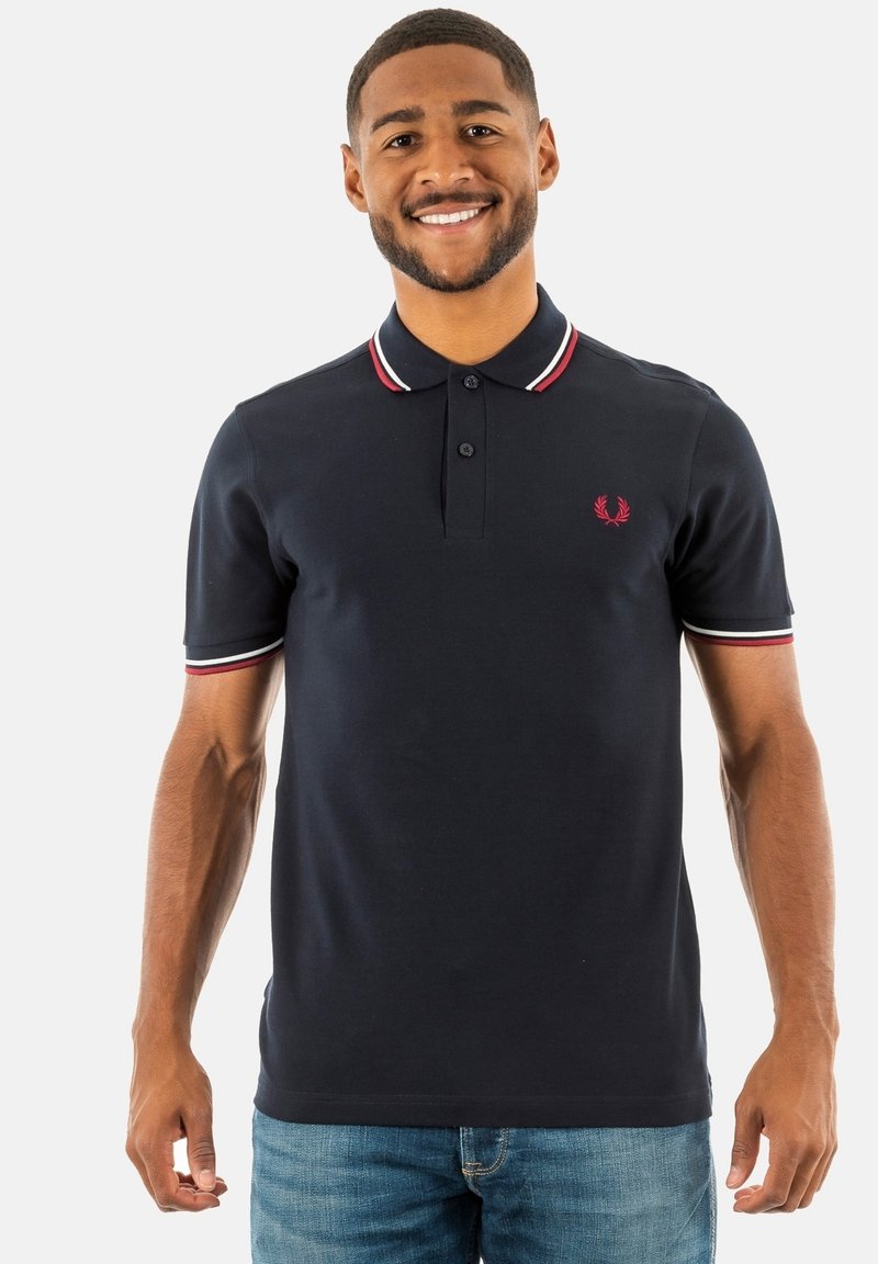 Mörkblå polo-shirt med tvåknappars placket, vit och röd randig krage, och broderad logotyp på bröstet. Mjuk bomullsmaterial.