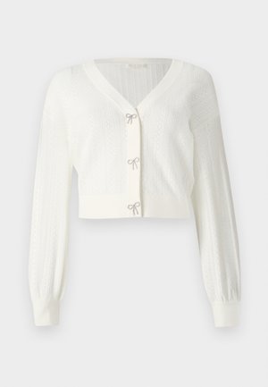 White cropped cardigan made of textured knit, featuring long puff sleeves and decorative bows at the front fastenings.