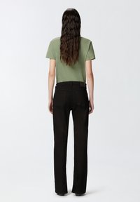 Camisa verde de manga corta combinada con pantalones vaqueros negros de pierna recta. El conjunto presenta un diseño simple y una tela texturada. Sin patrones o acentos visibles.
