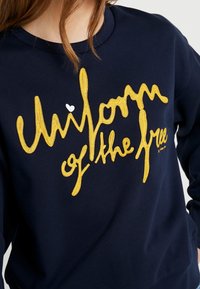 Felpa navy in cotone, con testo ricamato giallo "Children of the Free" e un piccolo dettaglio a forma di cuore bianco.