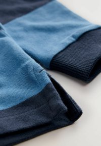 Primer plano de tela de punto azul y azul oscuro con puño acanalado y borde doblado sobre una superficie clara.