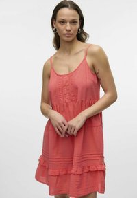 Vestido color coral de tejido ligero, con tirantes finos, un cuerpo con textura y un dobladillo acampanado con volantes.