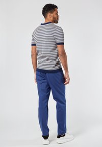 Suéter de punto a rayas con mangas cortas, en tonos azul y blanco, y cuello de canalé en navy, combinado con pantalones azules y zapatillas blancas.