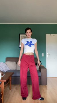 White cropped t-shirt with a blue flower graphic, paired with wide red trousers. Smooth fabric with a relaxed fit. Black shoes.