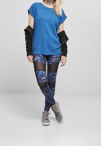 T-shirt azzurro a girocollo, strato esterno nero; leggings a fantasia blu e viola con inserti in mesh; sneaker alte grigie.