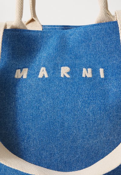Sac fourre-tout en denim bleu avec des poignées crème, ornée de lettres blanches brodées épelant "MARNI" sur le devant.
