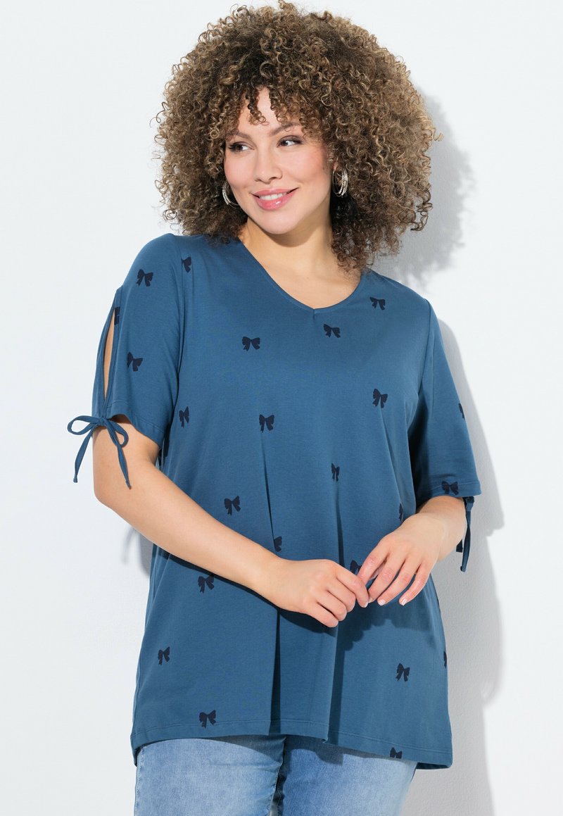 T-shirt bleu en V avec des manches courtes, présentant des motifs de nœuds noirs et des détails de liens sur les manches. Tissu doux avec une coupe ample.
