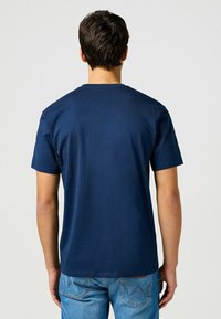 Camiseta de algodón azul marino de manga corta con cuello redondo, combinada con unos pantalones vaqueros denim azul claro que presentan costuras visibles en los bolsillos traseros.