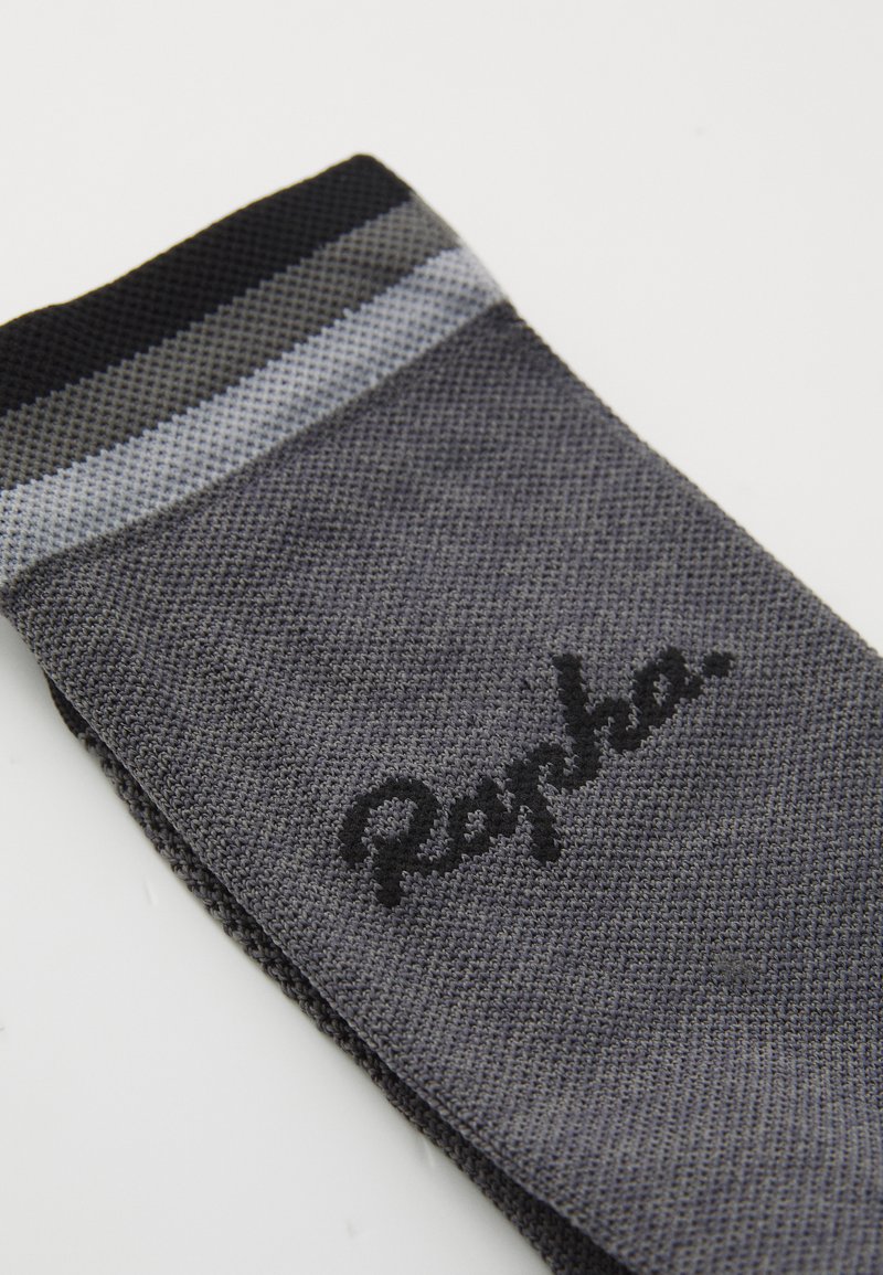 Chaussette de cyclisme grise avec un tissage texturé, présentant un poignet strié noir et gris clair et un logo "Rapha" brodé en noir.