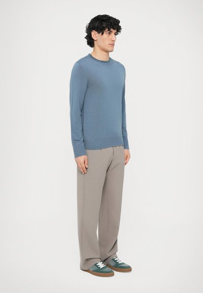 Jasnoniebieski sweter z długim rękawem, z prążkowanym, okrągłym dekoltem i ściągaczem u dołu. Do tego jasnoszare spodnie oraz zielono-szare trampki ze sznurowadłami w białym kolorze.