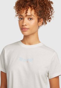White cotton t-shirt with short sleeves, featuring light blue floral embroidery and logo on the front. Smooth texture without additional patterns.