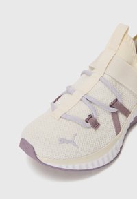 Lightweight, off-white mesh sneaker with lavender accents, elastic laces, and a textured sole. Features Puma logo on the side.