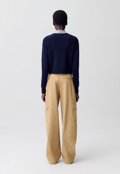 Un pull court navy et un pantalon cargo large beige clair. Le pull a un design classique ; le pantalon présente des poches latérales et une coupe décontractée.